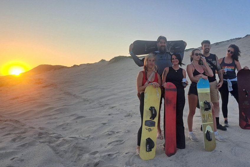 En gruppe mennesker på en strand med snowboard, solen går ned i baggrunden. 1