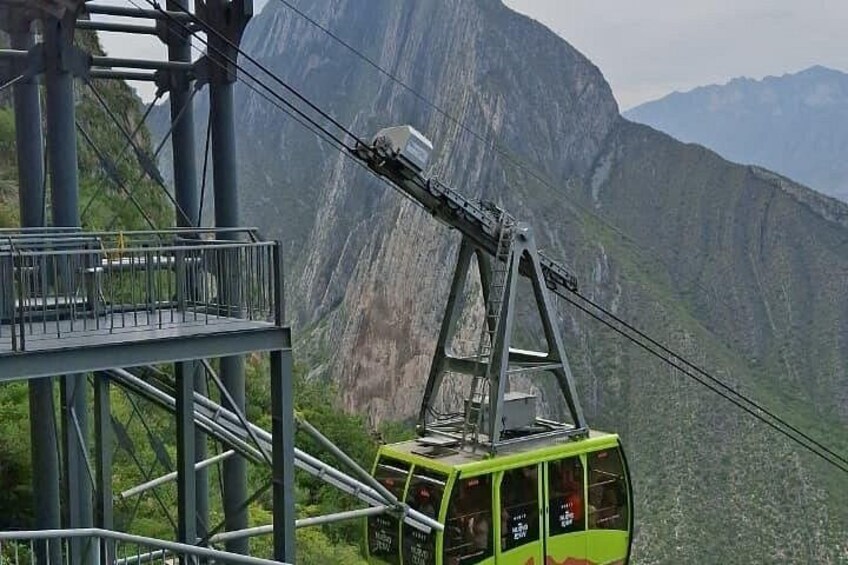 A cable car system with a green car suspended by cables against a mountainous backdrop. 2