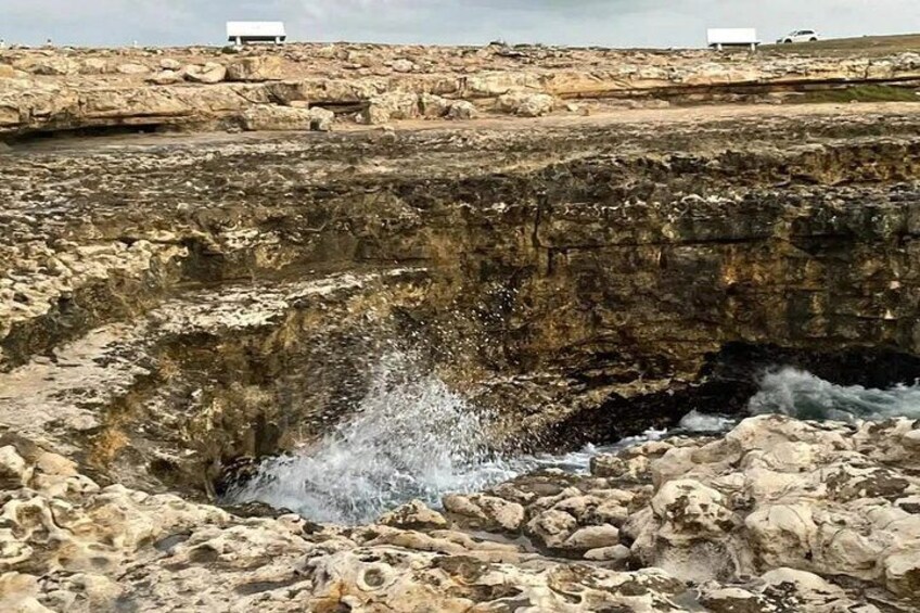 Een rotsachtig landschap met een grote sinkhole, spetters van water en verderop bewegende voertuigen. 2