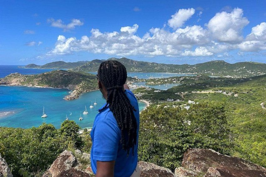 A person overlooking a coastal landscape with clear skies, green hills, and boats in the water. 2