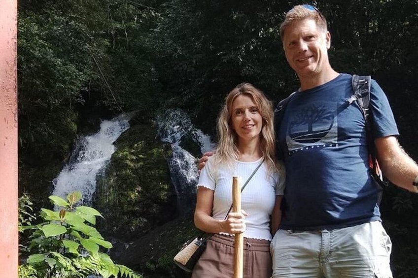A person standing in front of a waterfall with dense greenery in the background. 5