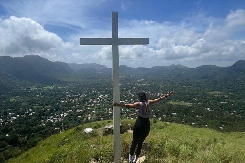 A person standing next to a large cross on a hill overlooking a valley. 3