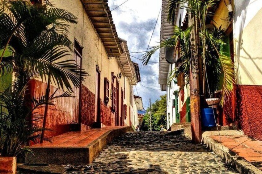 A narrow cobblestone street flanked by buildings with red and white facades, palm trees, and a clear sky. 5