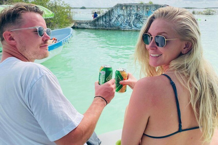 Two people holding drinks by a body of water with a bridge in the background. 4