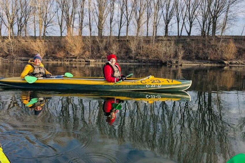 Two people kayaking on a calm river with reflections of trees and a clear sky. 4