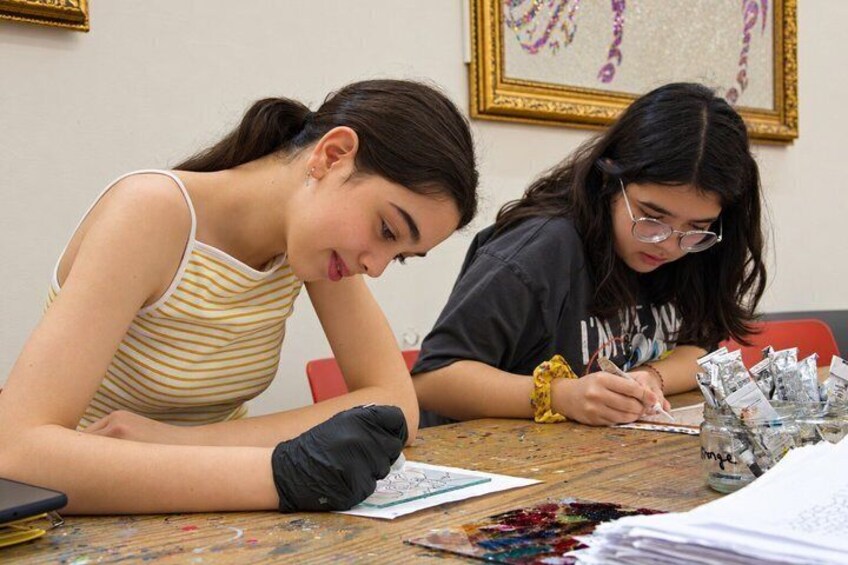 Two individuals seated at a table with art supplies, engaged in a creative activity. 4