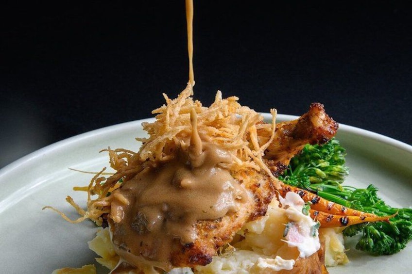 A plate with a grilled chicken leg, a creamy sauce, shredded topping, and a side of broccoli. 3