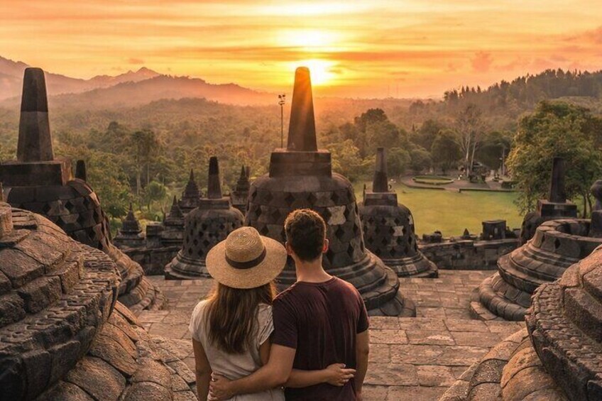 A couple standing on a stone pathway with ancient stone structures and a sunset in the background. 1