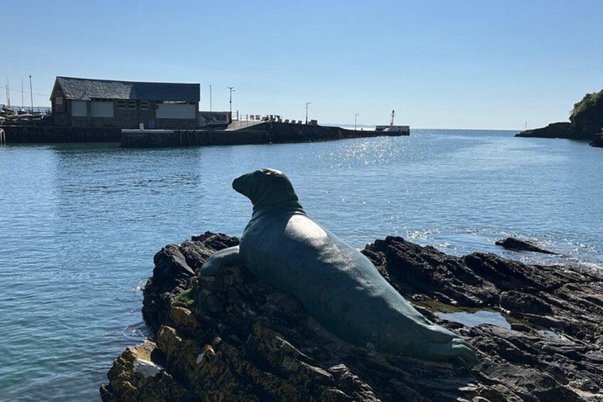 Una statua a forma di foca su rocce, vicino a un'acqua calma, con un edificio sullo sfondo. 4