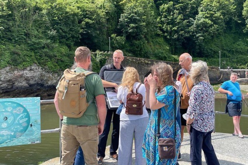 Un groupe de personnes se tient près d’une étendue d’eau, certaines avec des sacs à dos, à proximité d’un panneau d’affichage. 3