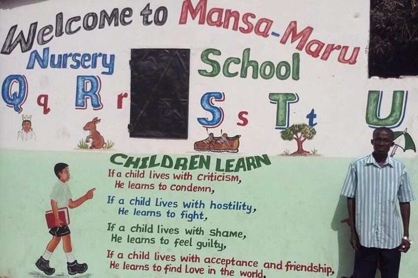 A welcome sign for Mansa-Maru Nursery School with a child learning illustration and a man standing beside it. 1