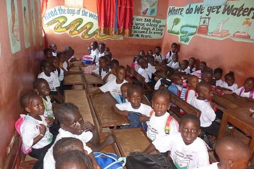 A classroom with children seated at desks, a calendar on the wall, and educational posters. 4