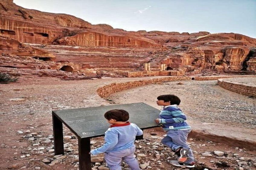 Two children examining a sign in a rocky desert landscape with layered rock formations. 4