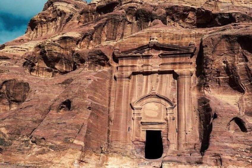 A carved rock facade with a central doorway and columns, set against a rugged mountainous backdrop. 2