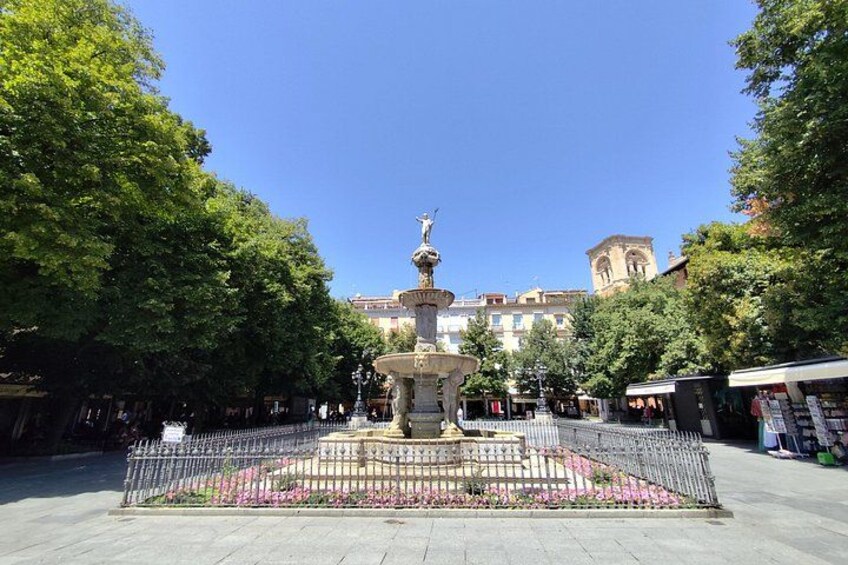 Una fontana con una statua al centro, circondata da un recinto e fiori. 2