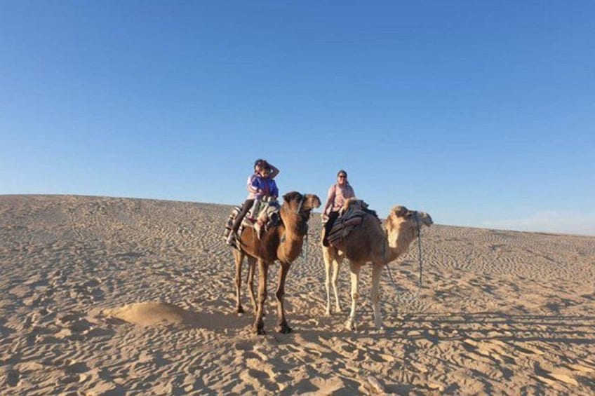 Two camels with riders in a desert landscape. 1