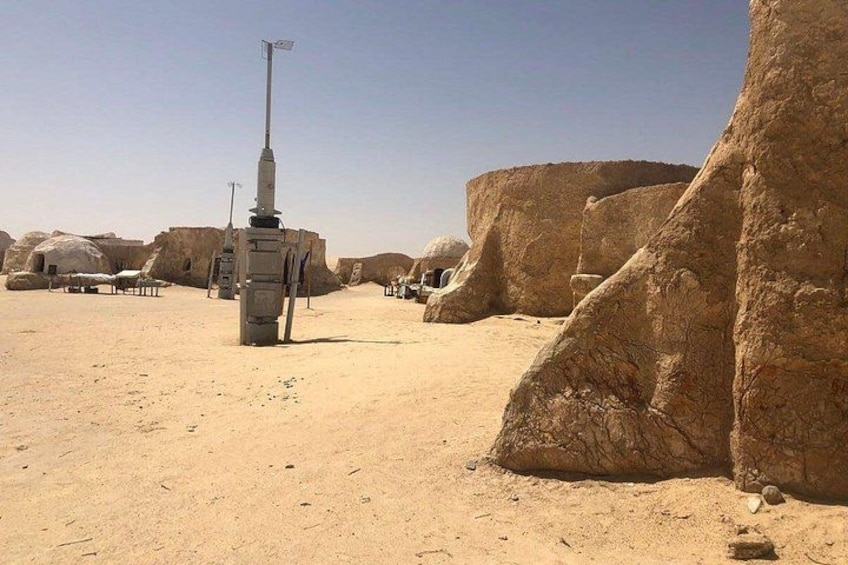 A desert landscape with large rock formations and a tall, narrow structure in the center. 2
