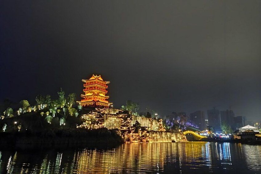 A brightly lit pagoda at night with reflections on water, surrounded by trees and buildings. 5