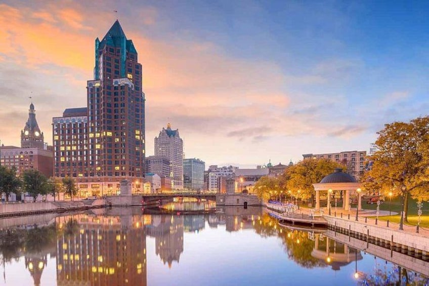 A cityscape with a prominent building reflecting in a calm river, a bridge, and a gazebo. 2