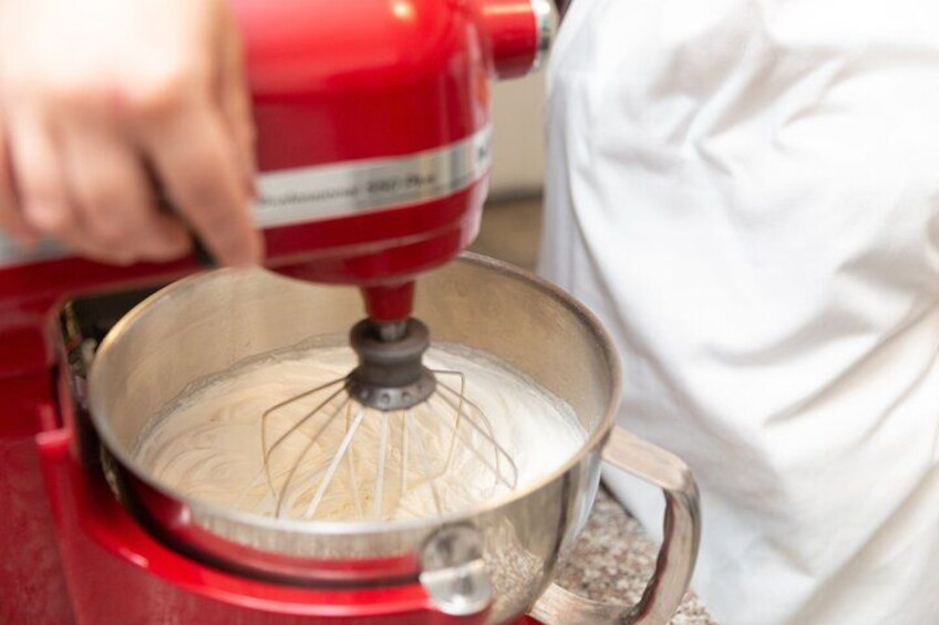 Een hand gebruikt een rode KitchenAid mixer om ingrediënten te mengen in een metalen kom. 4