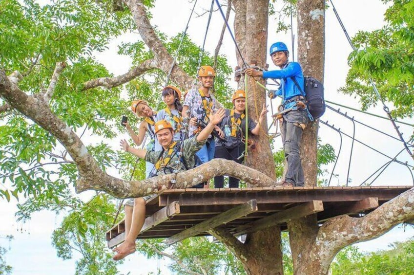 A group of people on a wooden platform in a tree, wearing helmets and harnesses, engaged in an outdoor activity. 4