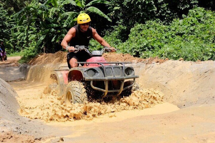 A person riding a red ATV through a muddy path. 1