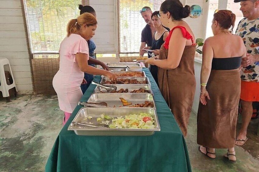 A buffet setup with food trays and people serving and selecting food. 3