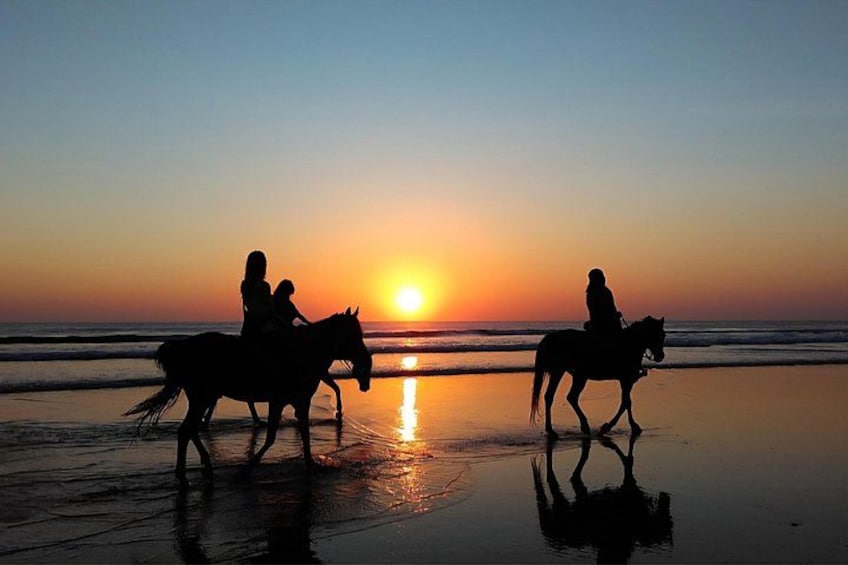 Les silhouettes de deux personnes à cheval sur une plage au coucher du soleil. 2