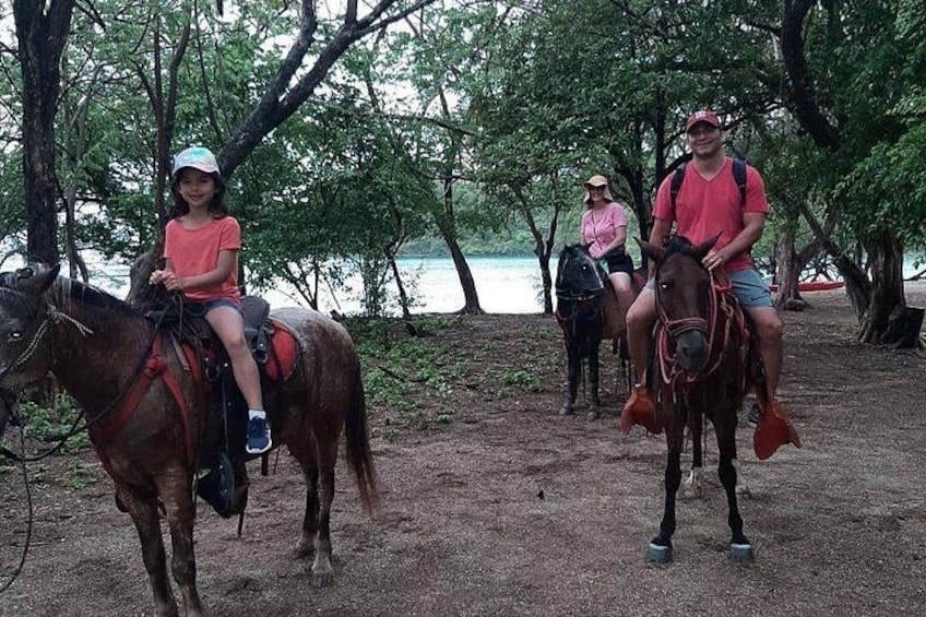 Trois personnes à cheval, sur un chemin de terre bordé d’arbres. 1