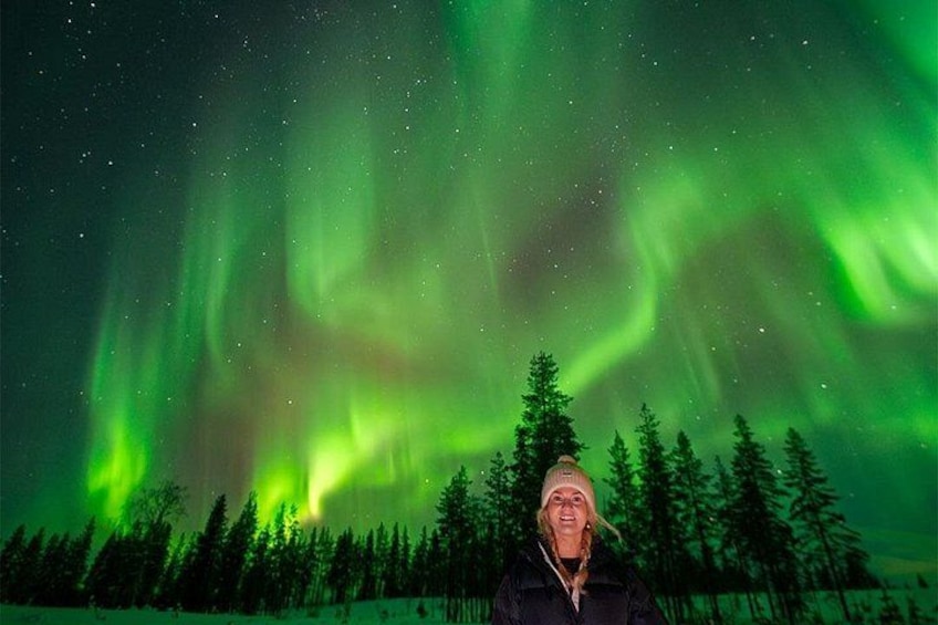 A person standing in a forest with the Northern Lights in the background. 1