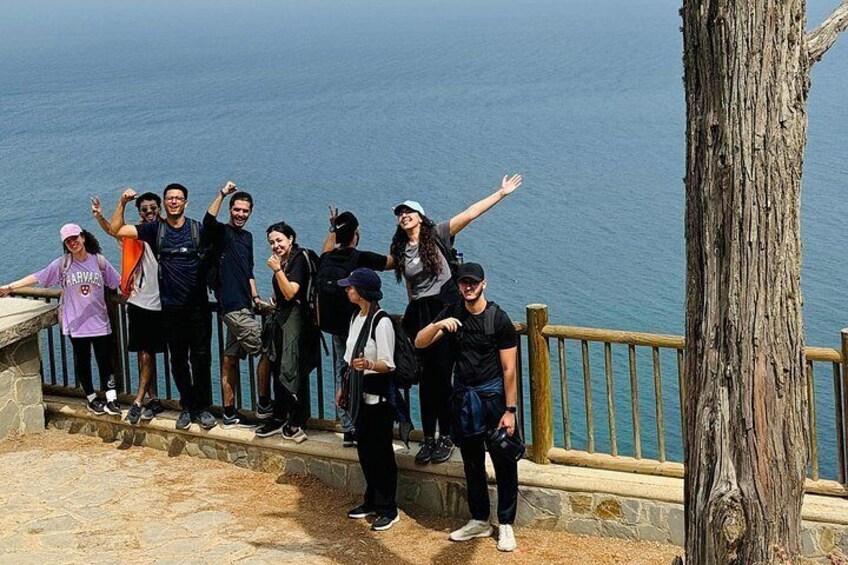 Un grupo de personas sobre una plataforma de piedra al borde del mar, con una baranda de madera y un tronco de árbol a la vista. 1
