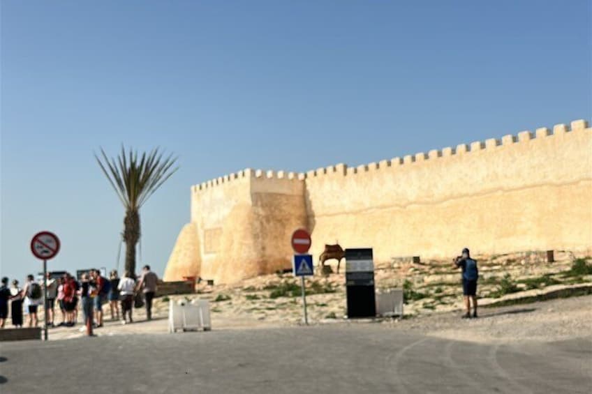 A historical fortification with tourists, a palm tree, and a no parking sign. 2
