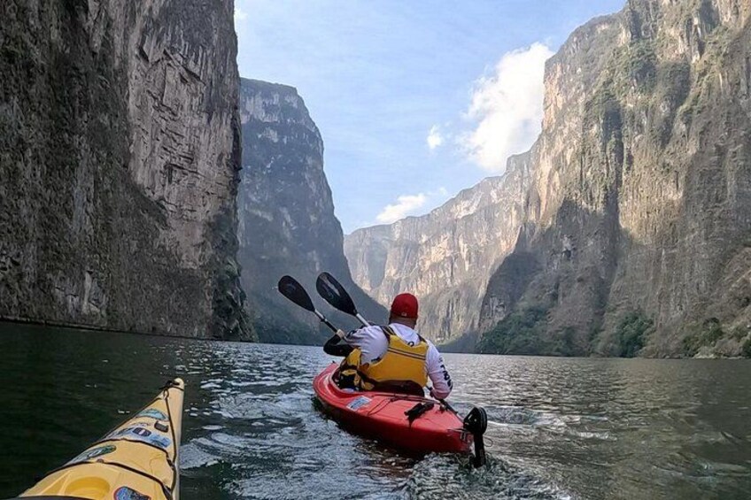 A person kayaking on a river with steep cliffs on both sides. 1