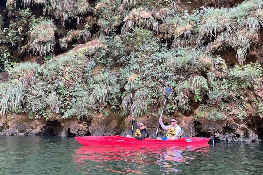 Two people in a red kayak on a calm river, surrounded by lush greenery and rocky terrain. 3