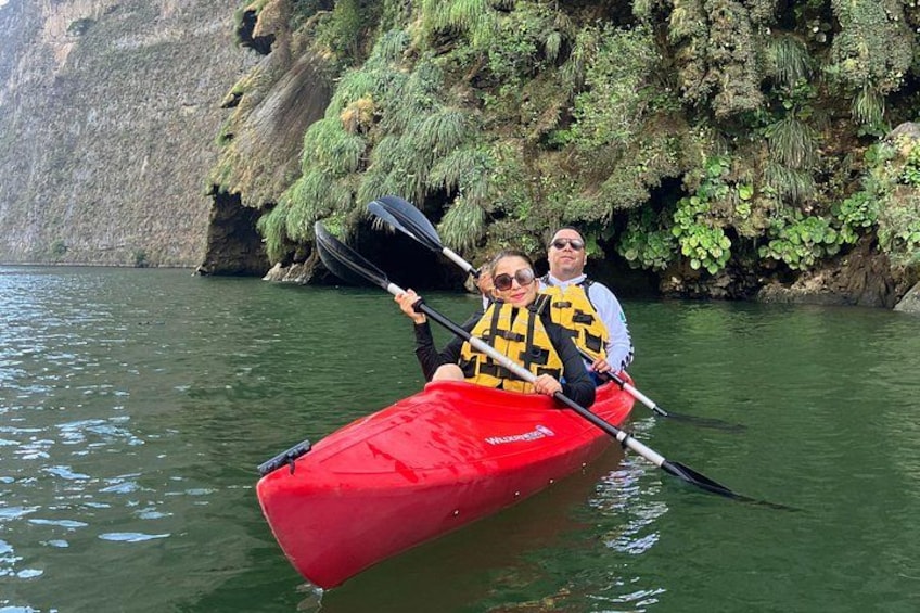 Two people in a red kayak on a calm river with rocky cliffs in the background. 2