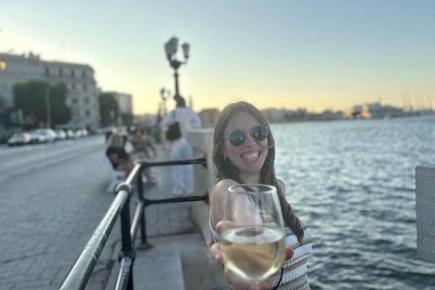 A person holding a glass of white wine, a waterfront, and a cityscape with buildings and a statue in the background. 2