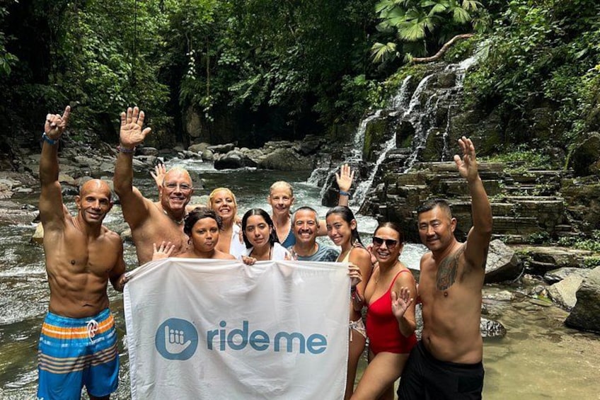 A group of people posing in front of a waterfall with a banner. 1