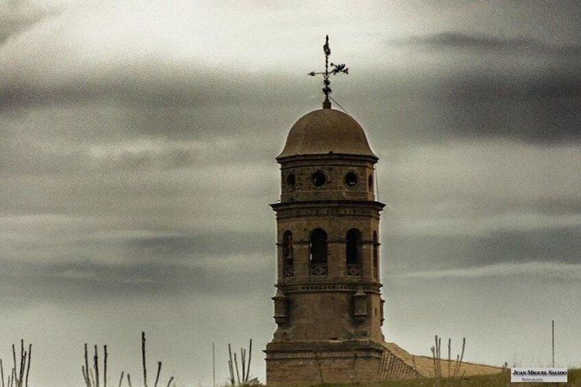 Un campanario solitario con veleta en la parte superior, sobre un cielo nublado. 2