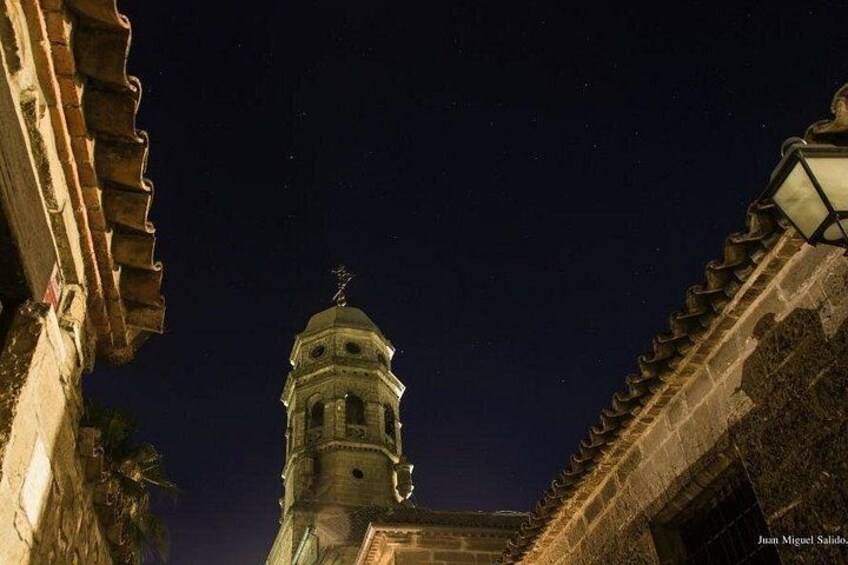 Una escena nocturna con una torre iluminada y un edificio de tejado a la vista. 5