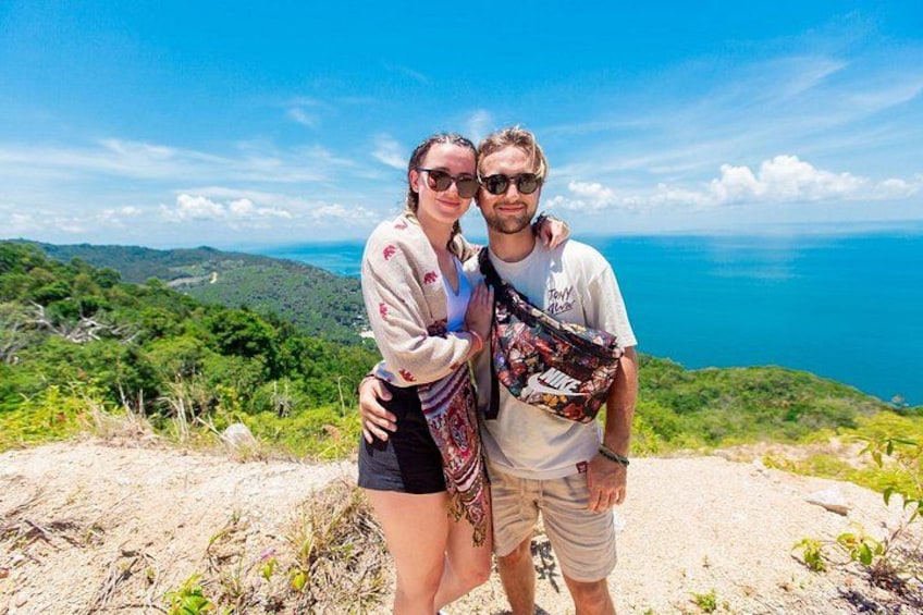 Two people standing on a hill with a view of the ocean and green hills in the background. 5