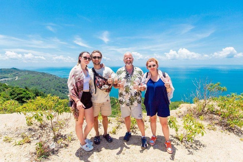 Four people standing on a rocky outcrop with a view of the ocean and hills in the background. 2