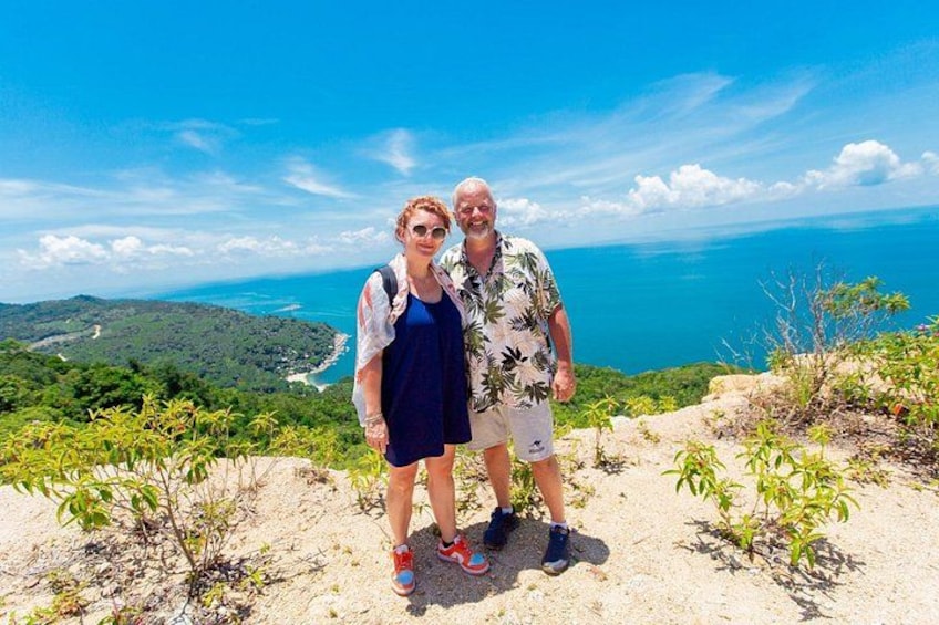 Two people standing on a sandy beach with a view of the ocean and greenery in the background. 4