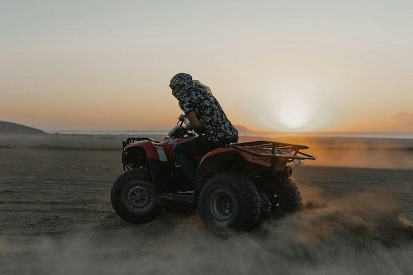 Eine Person fährt bei Sonnenuntergang mit einem Quad durch eine Wüstenlandschaft. 3