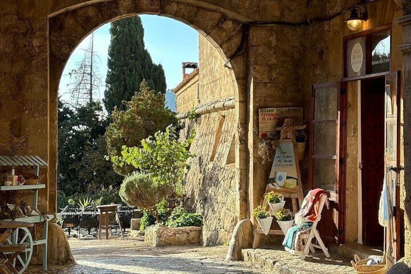 Un vieux bâtiment en pierre avec une porte en bois, une enseigne et un petit jardin agrémenté d’un arbre et d’un banc. 5