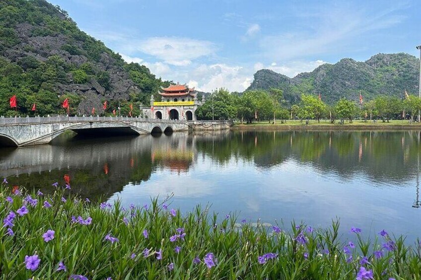 A bridge over a calm lake with a traditional building in the background. 2