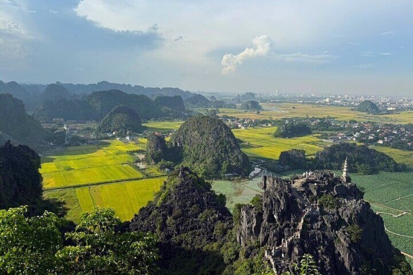 A mountainous landscape with green fields, rocky outcrops, and a distant city. 5