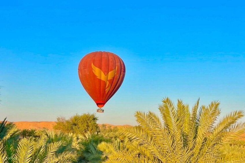 Un globo aerostático con diseño amarillo volando sobre un paisaje de palmeras y colinas rojas. 2