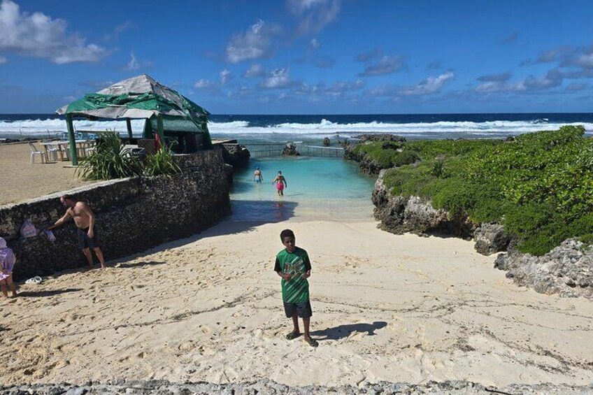 A beach with a man in a green shirt standing on the sand, a small hut, and a clear blue sky. 4