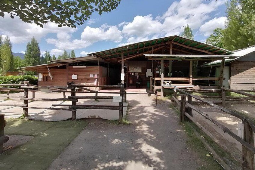 A rustic wooden building with a covered porch, picnic tables, and a dirt path. 3