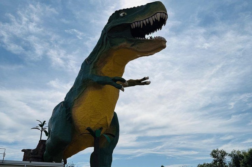 A large dinosaur statue with its mouth open, set against a cloudy sky. 5